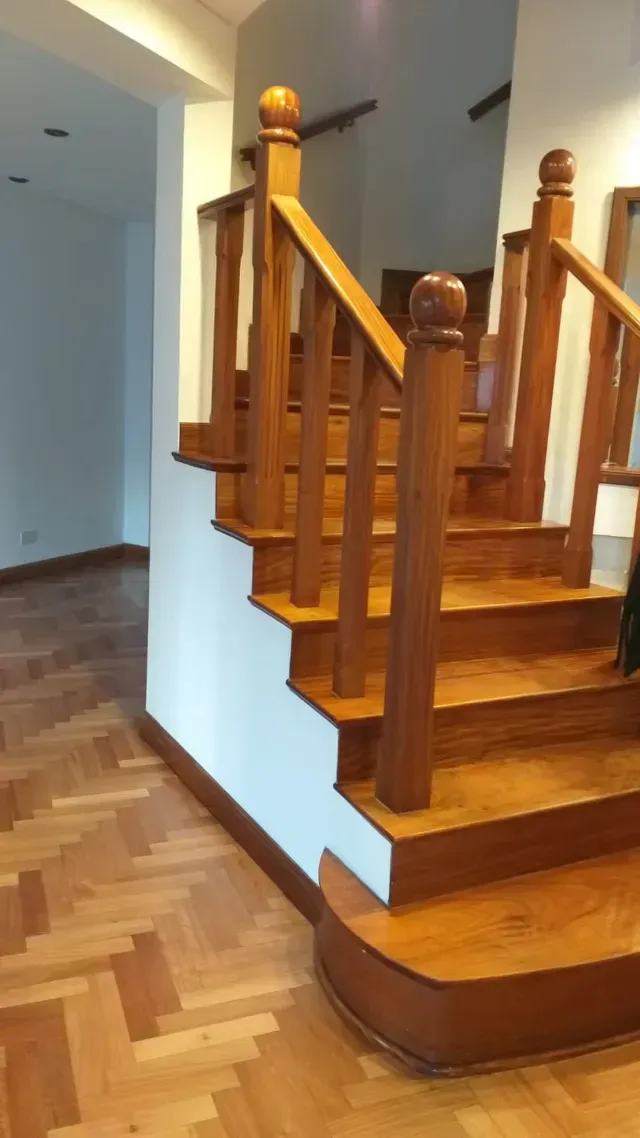 Escalera de madera con barandilla pulida y suelo de parqué en un luminoso pasillo interior.