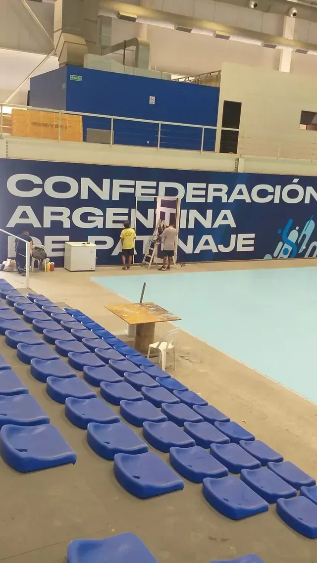Estadio cubierto con gradas azules y una gran pancarta que dice “Confederación Argentina de Balonmano”.