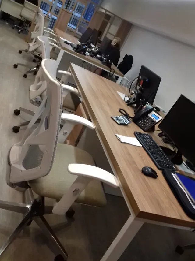 Espacio de oficina vacío con filas de escritorios, sillas blancas y monitores de computadora.