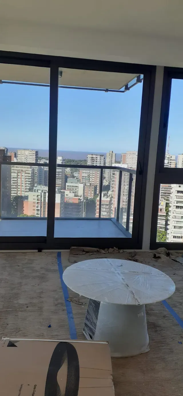 Habitación en un rascacielos con ventanales del suelo al techo, vistas al horizonte de la ciudad y una mesa redonda blanca.