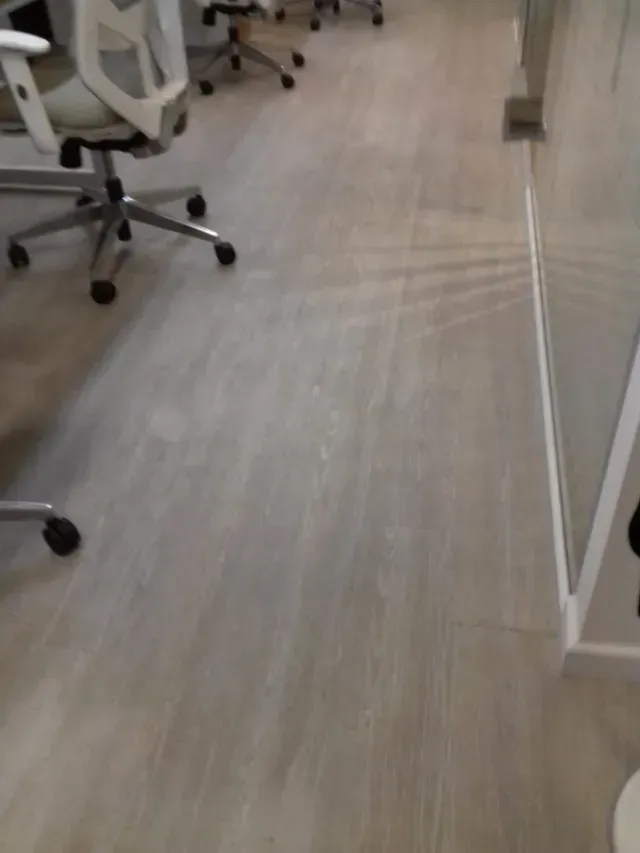 Pasillo de oficina con sillas con ruedas y suelo de madera clara.