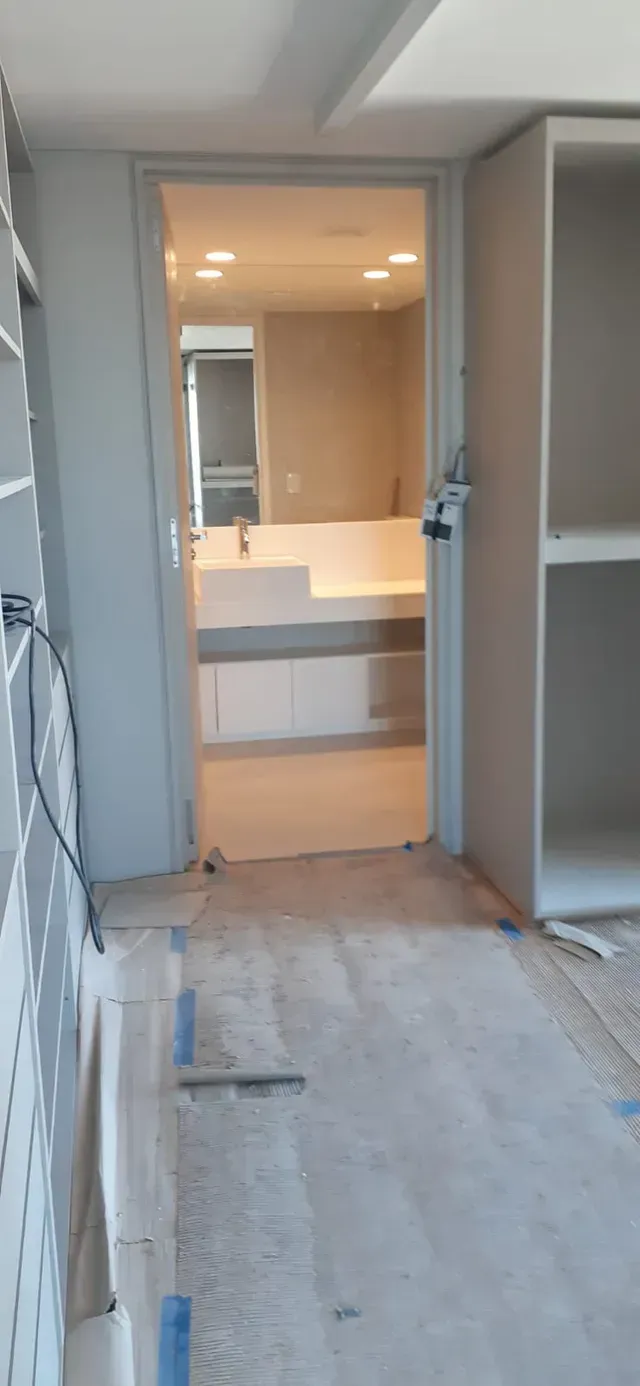 Baño parcialmente renovado con tocador blanco, espejo y suelo a la vista en un hueco del pasillo.