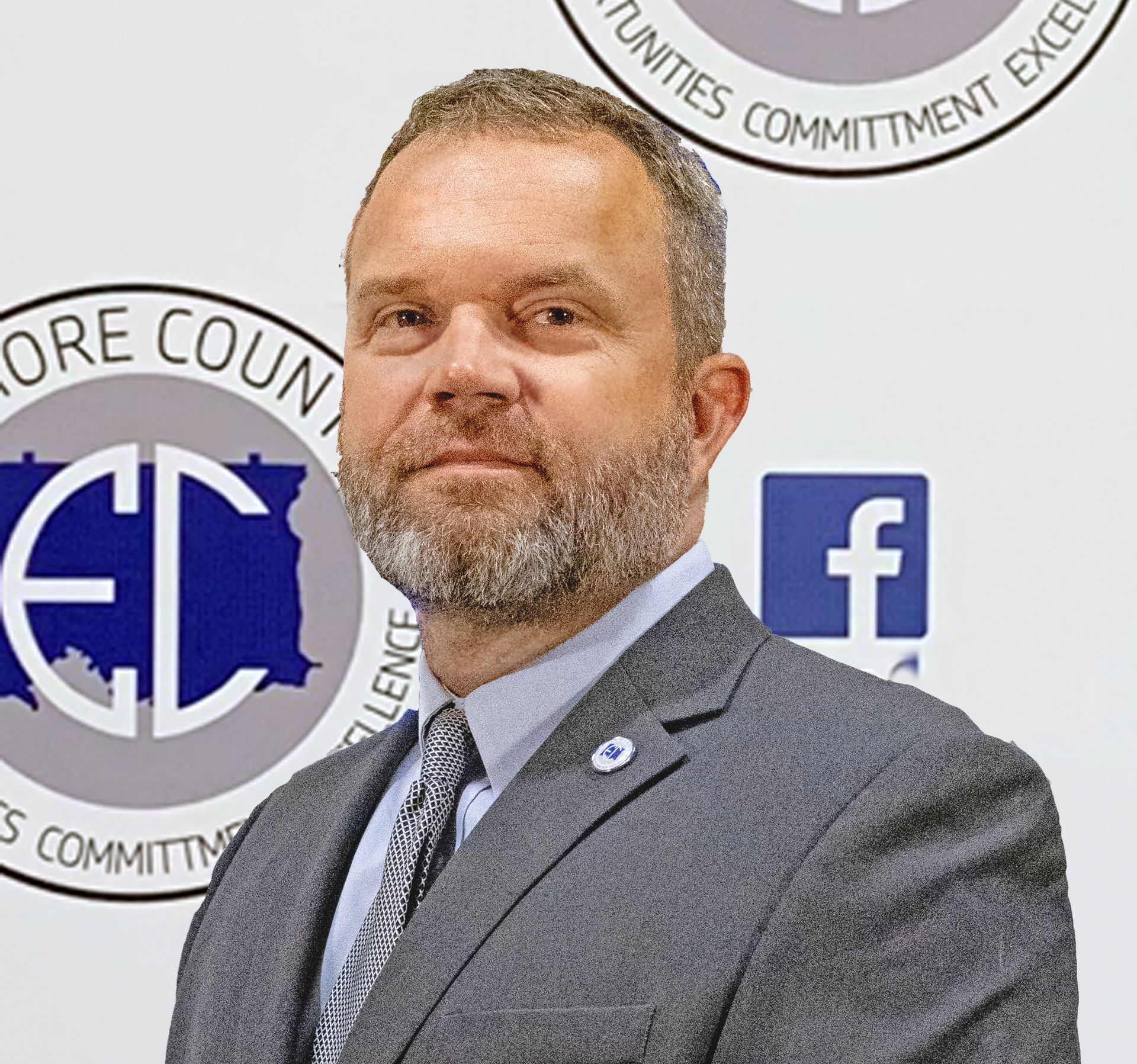 Man in a suit with a gray beard, in front of a Moore County logo. He is wearing a blue shirt and a patterned tie.