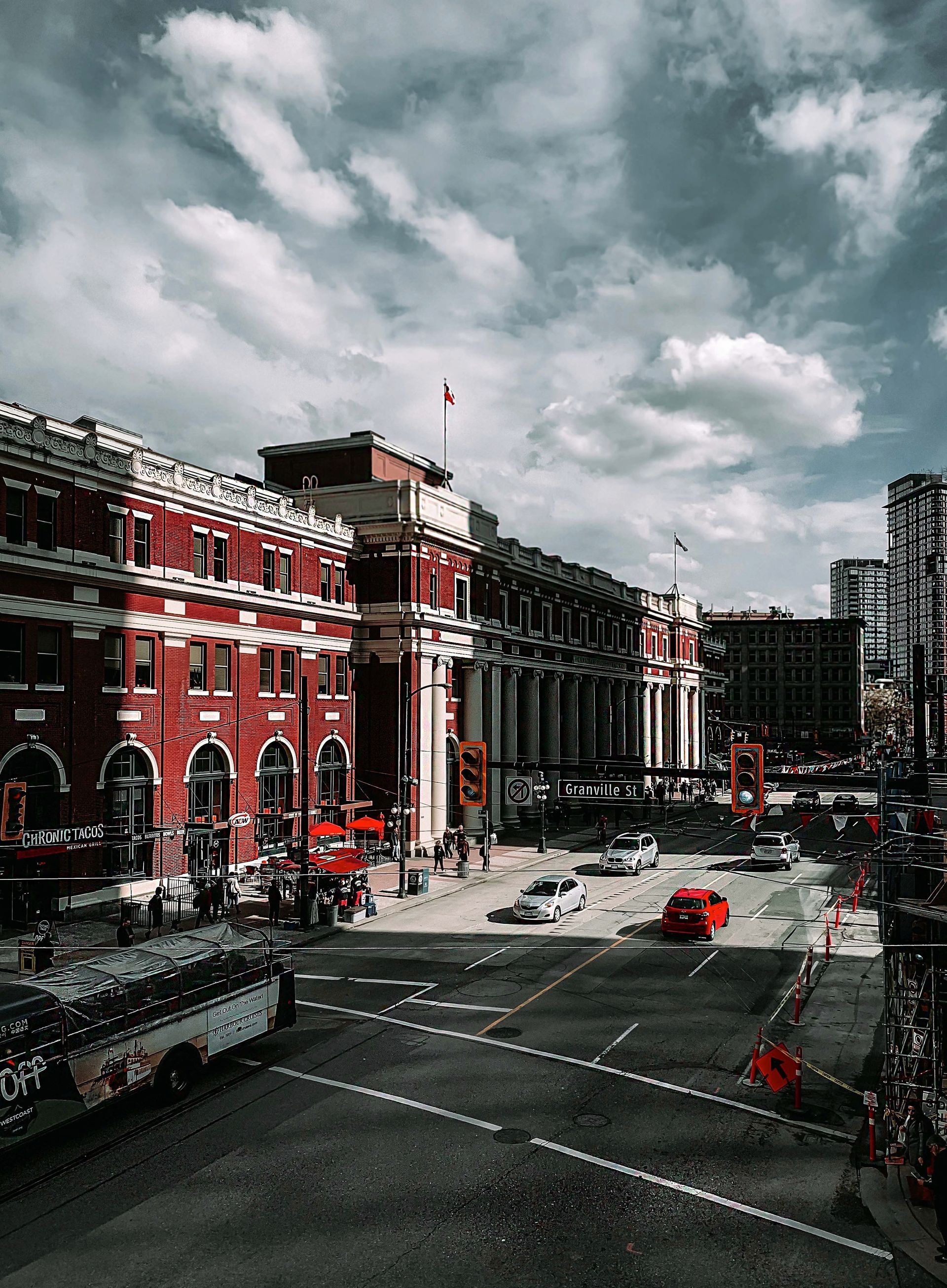 Red brick building with white accents, cars, and pedestrians on a street under a cloudy sky.