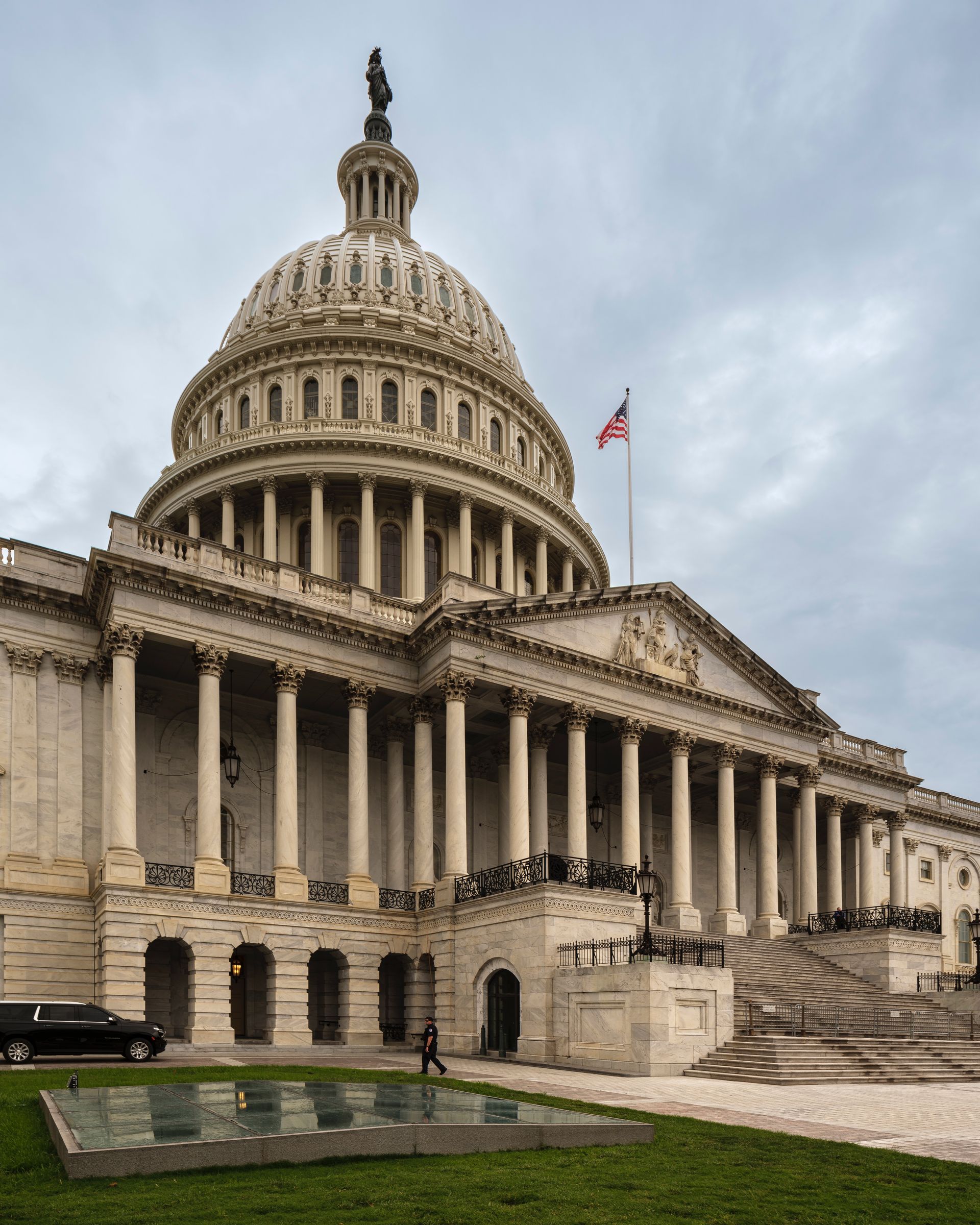 United States Capitol Building in Washington, D.C. A large neoclassical building with a dome, flag, and cloudy sky.