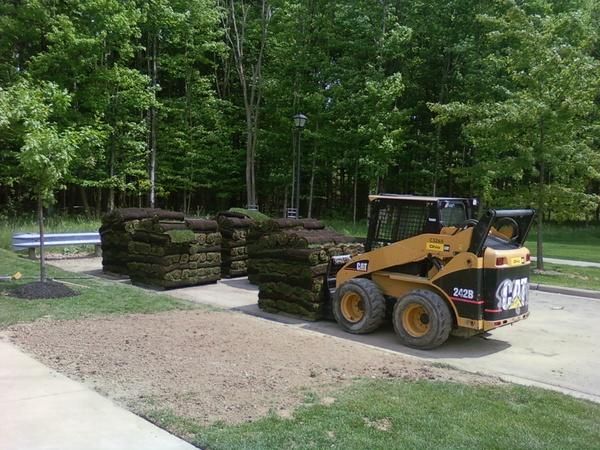 Yellow skid steer transporting stacks of sod.