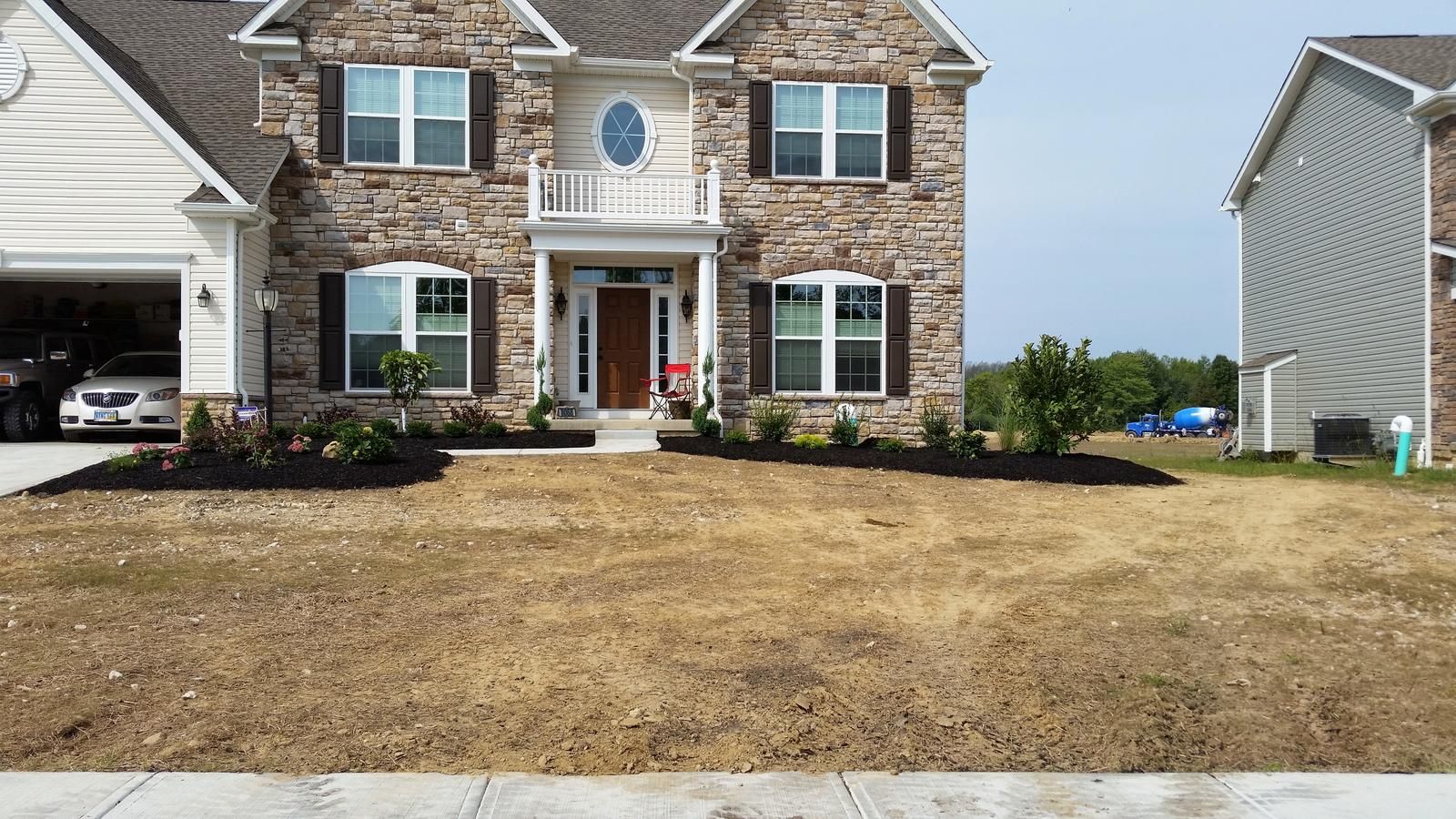 Two-story house with brick and siding, brown lawn, dark mulch in front of bushes.