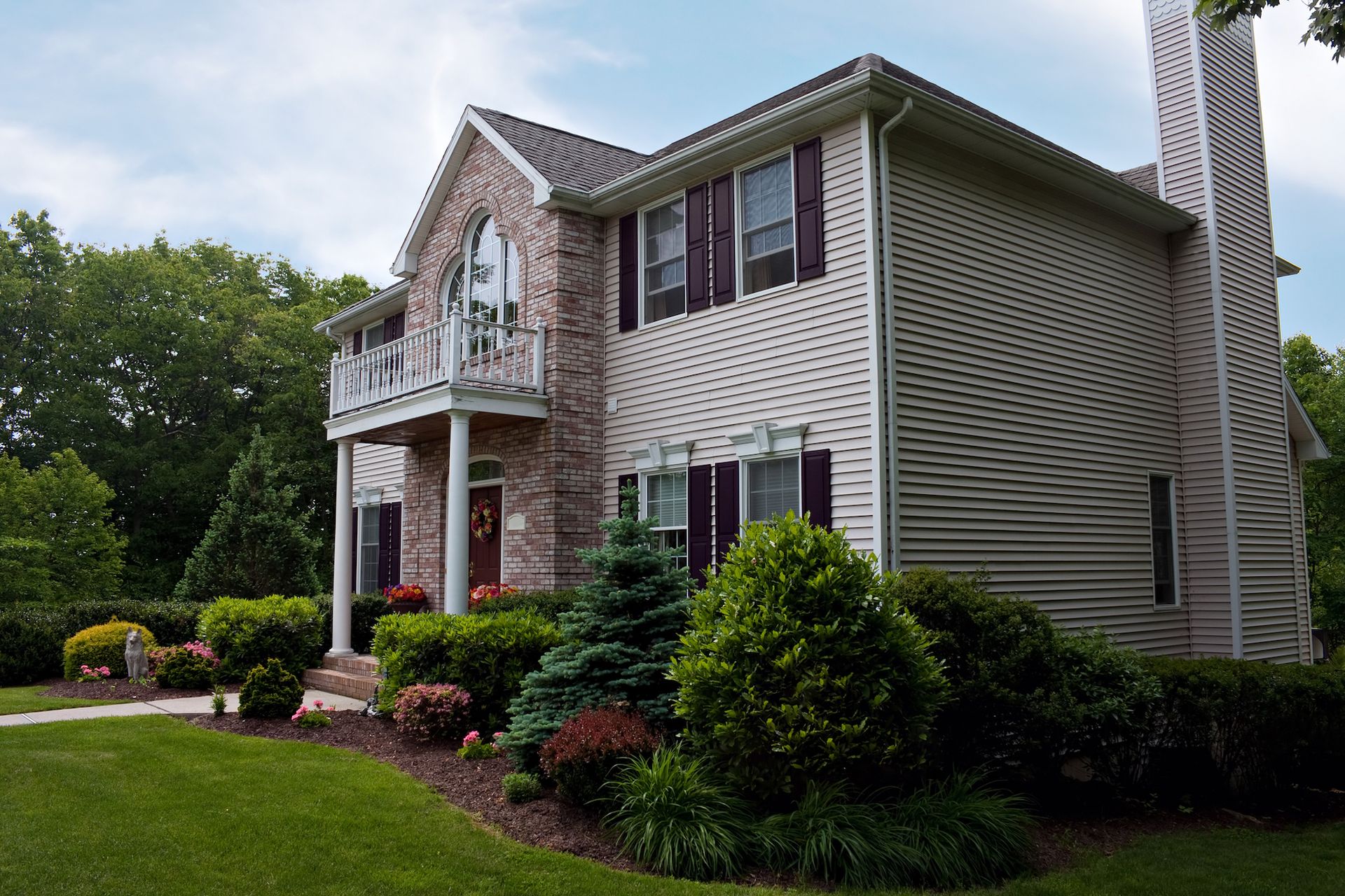 Two-story house with brick facade, beige siding, burgundy shutters, and landscaped yard.