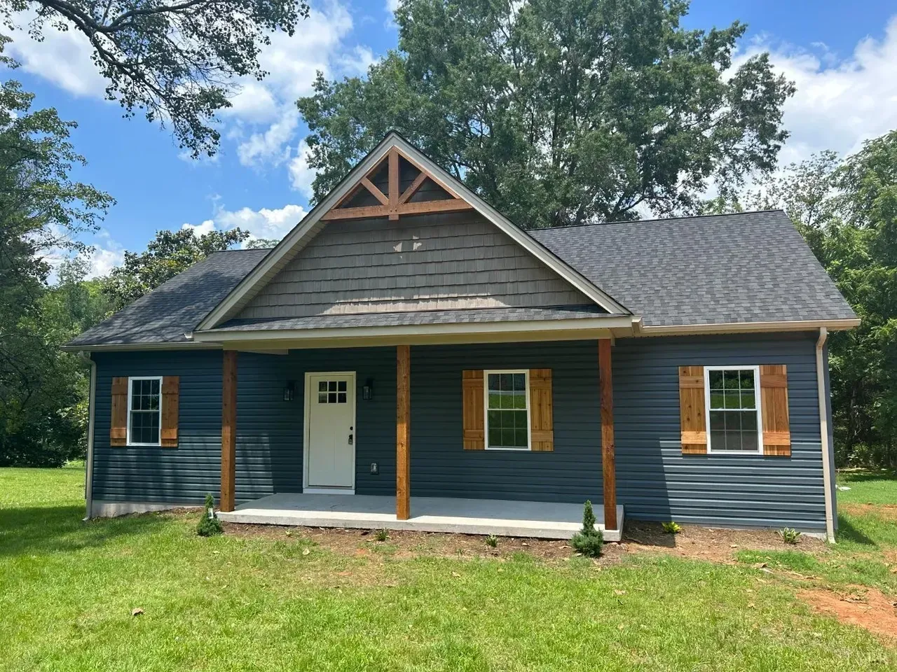 A single-story blue house with a covered front porch, white door, wooden shutters, and a dark shingled gable roof.