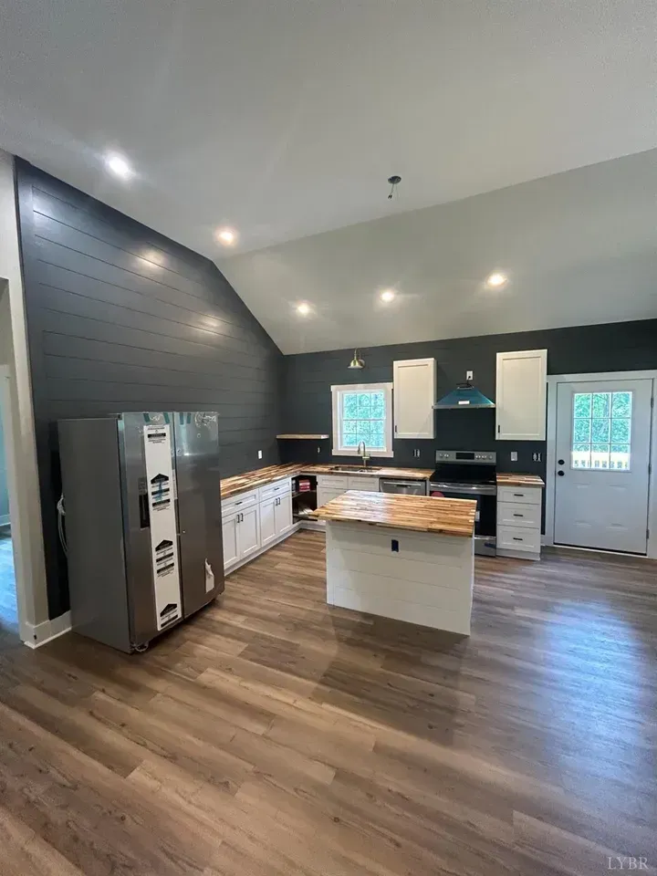 A spacious kitchen with white cabinets, a light wood-topped island, dark shiplap walls, and wood-look flooring.
