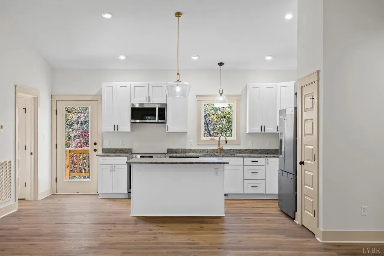 A bright, modern kitchen with white cabinets, gray granite countertops, a center island, and wood flooring.