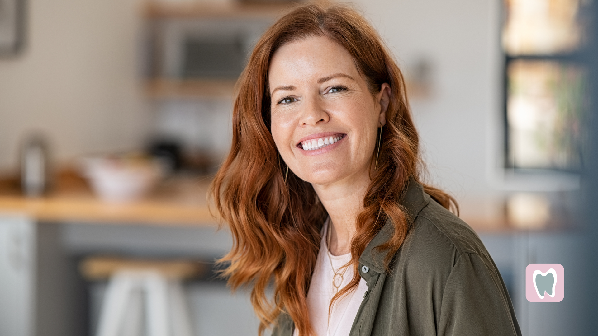 Woman with red hair smiling in a kitchen. She wears a green jacket.