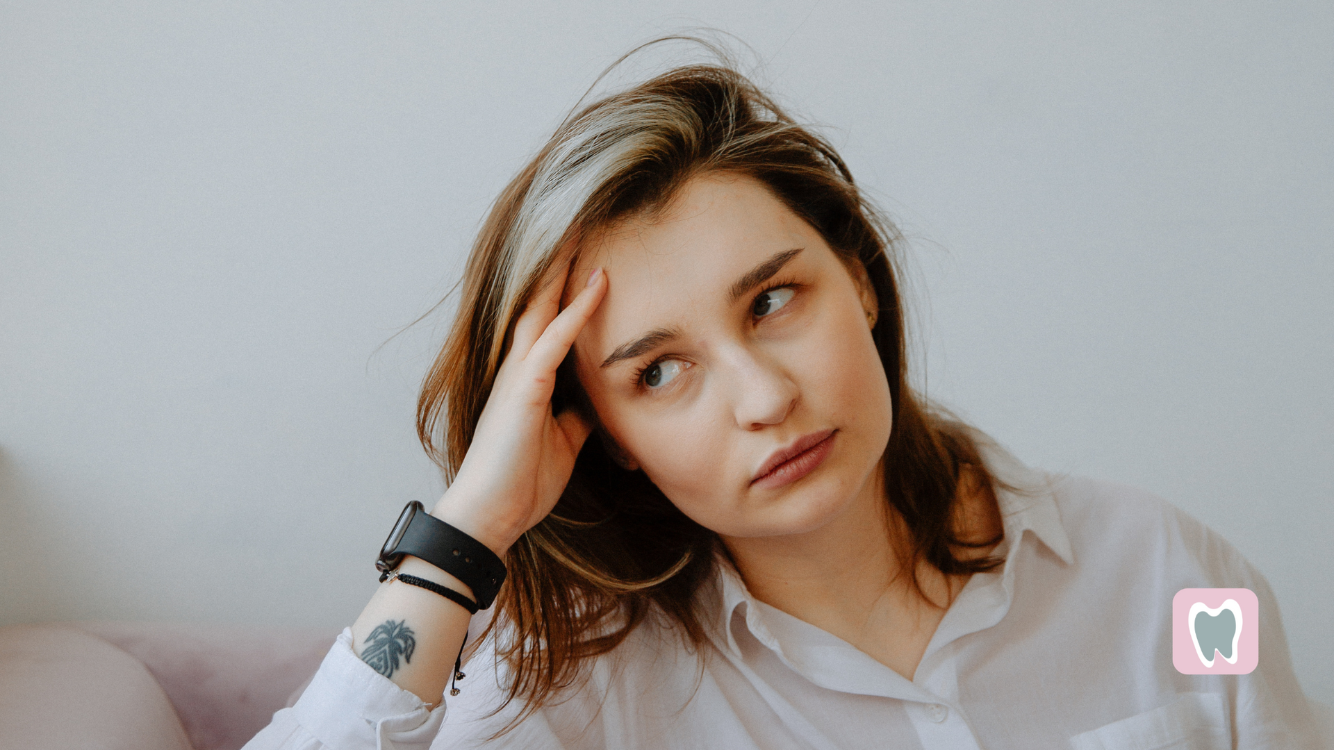 A woman is sitting on a couch with her hand on her forehead.