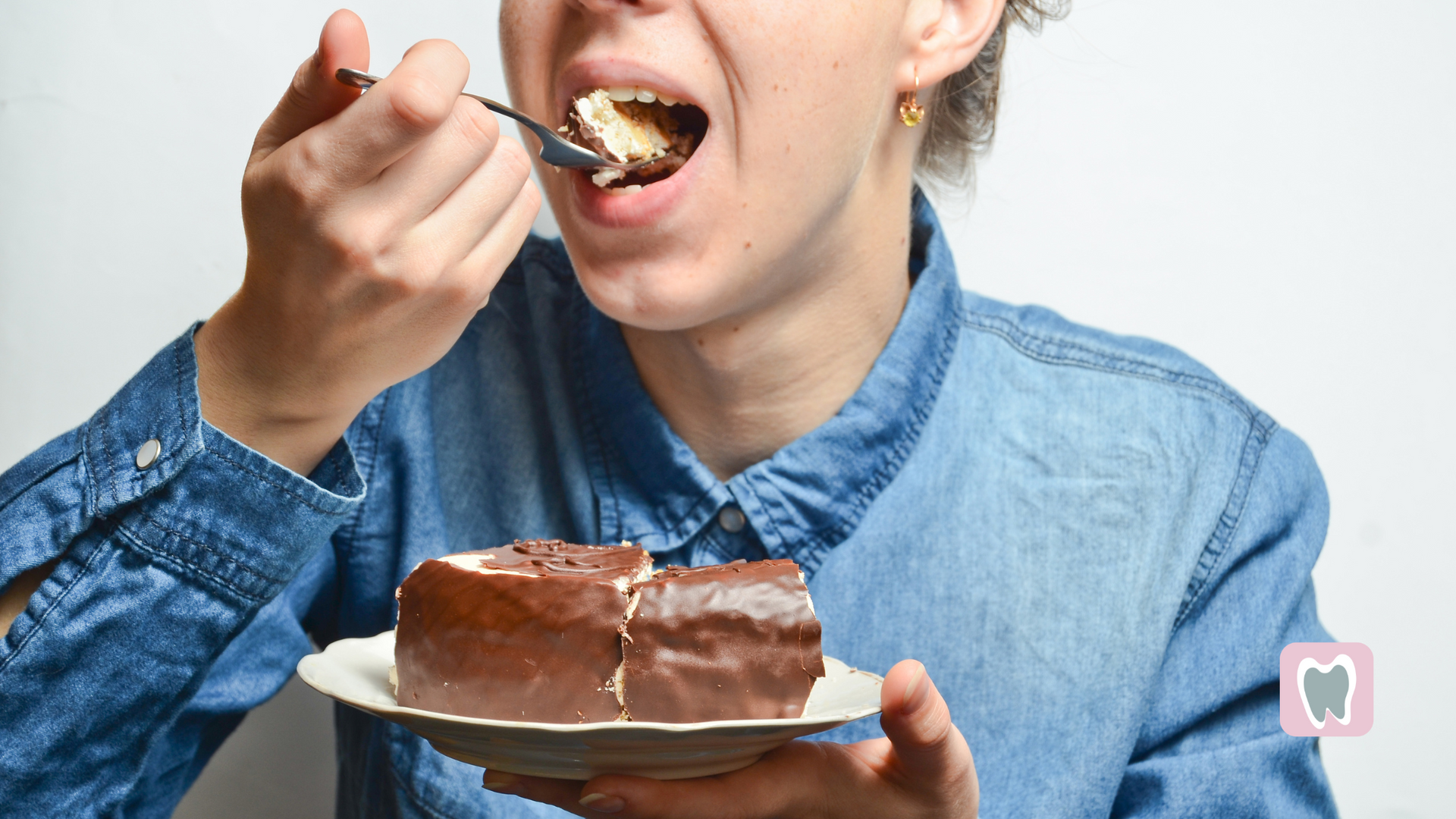 Woman eating cake, wearing a blue shirt, with a white plate.
