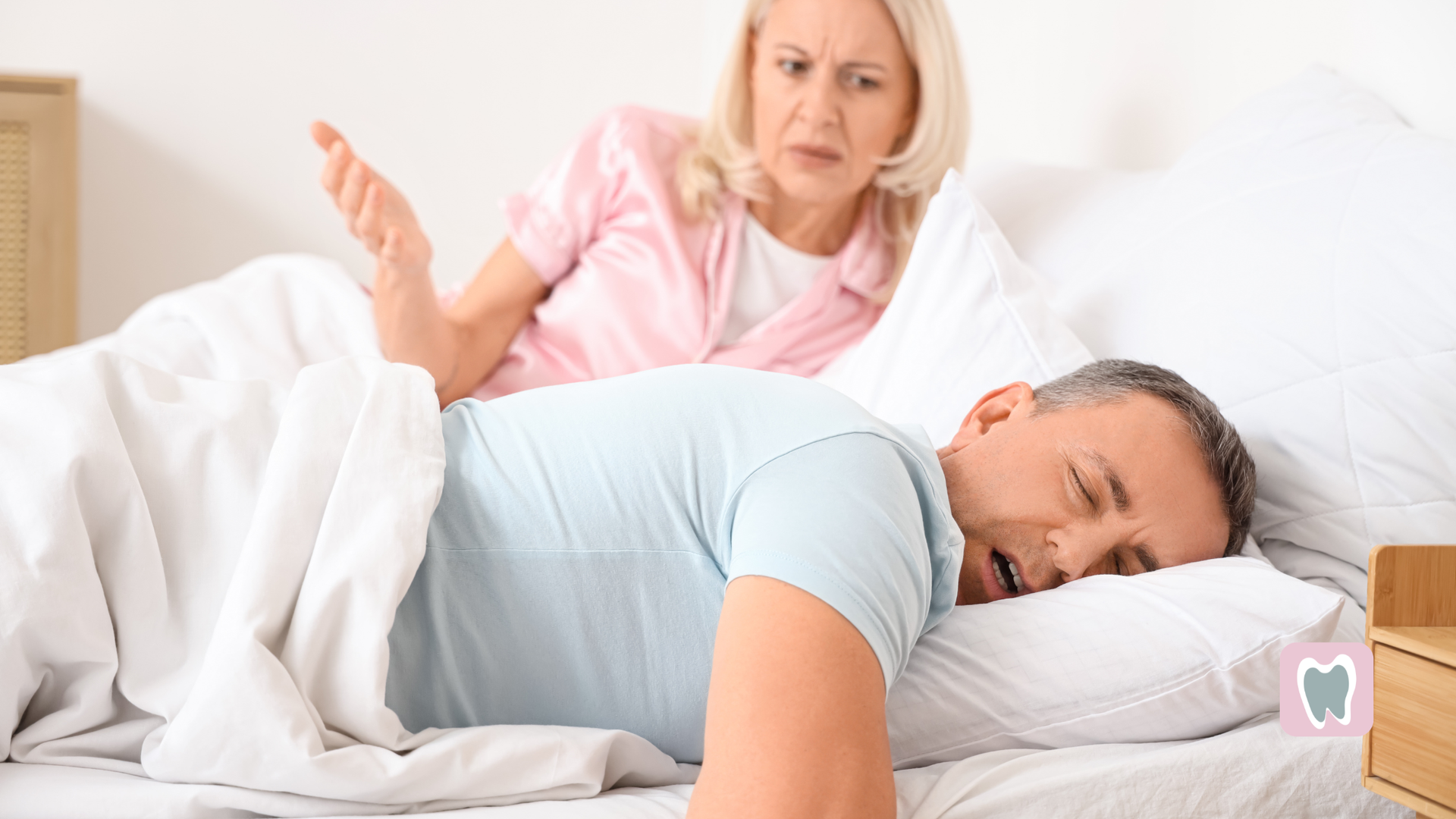 Woman looks concerned as man sleeps on bed in white bedroom, with another person sitting nearby.