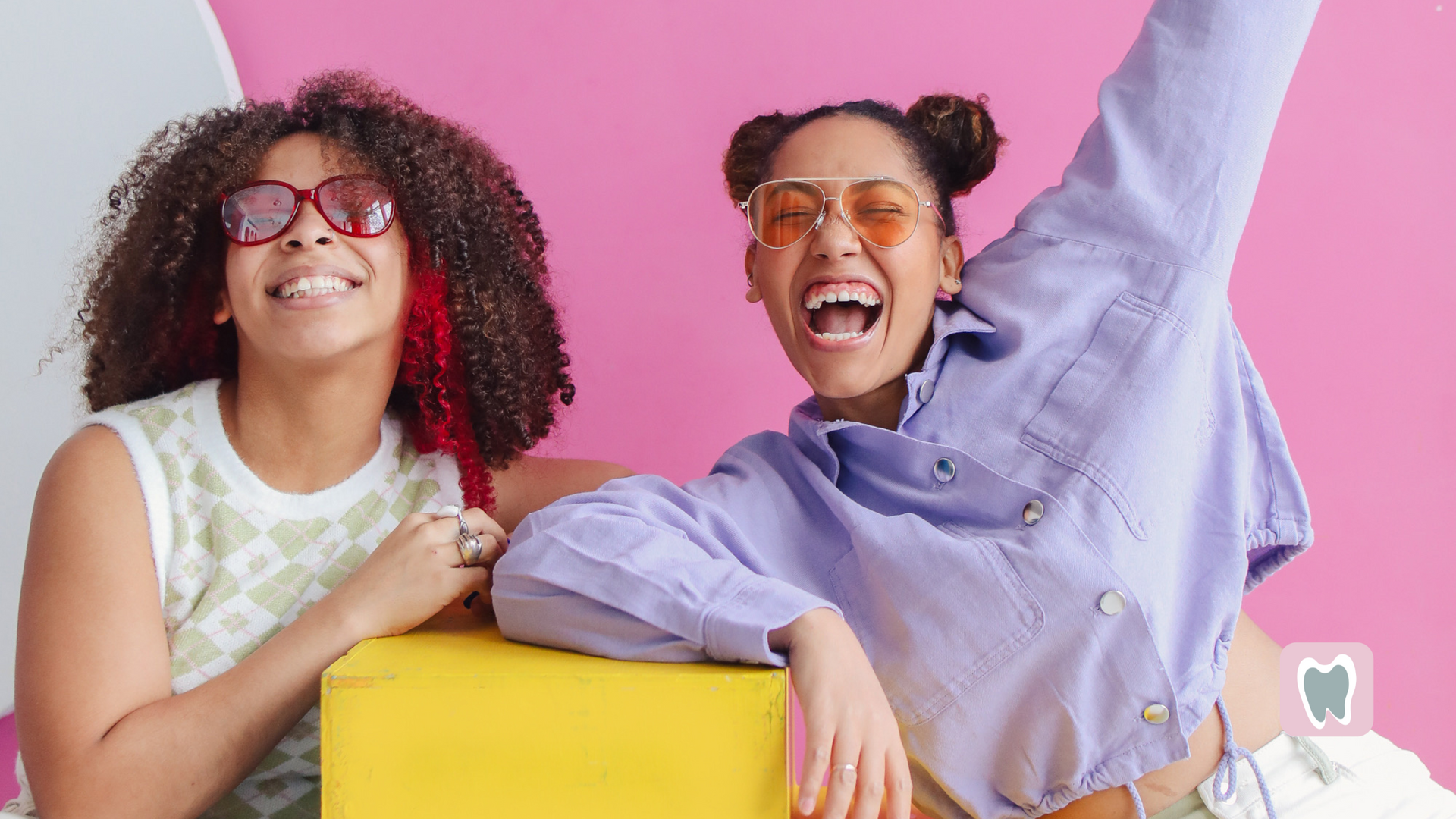 Two women are sitting next to each other on a yellow block.