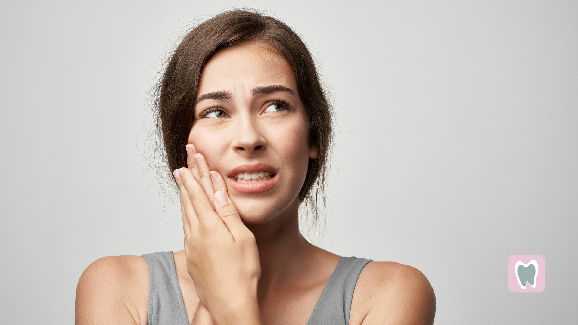 Woman touching her cheek with a worried expression, on a plain light background.
