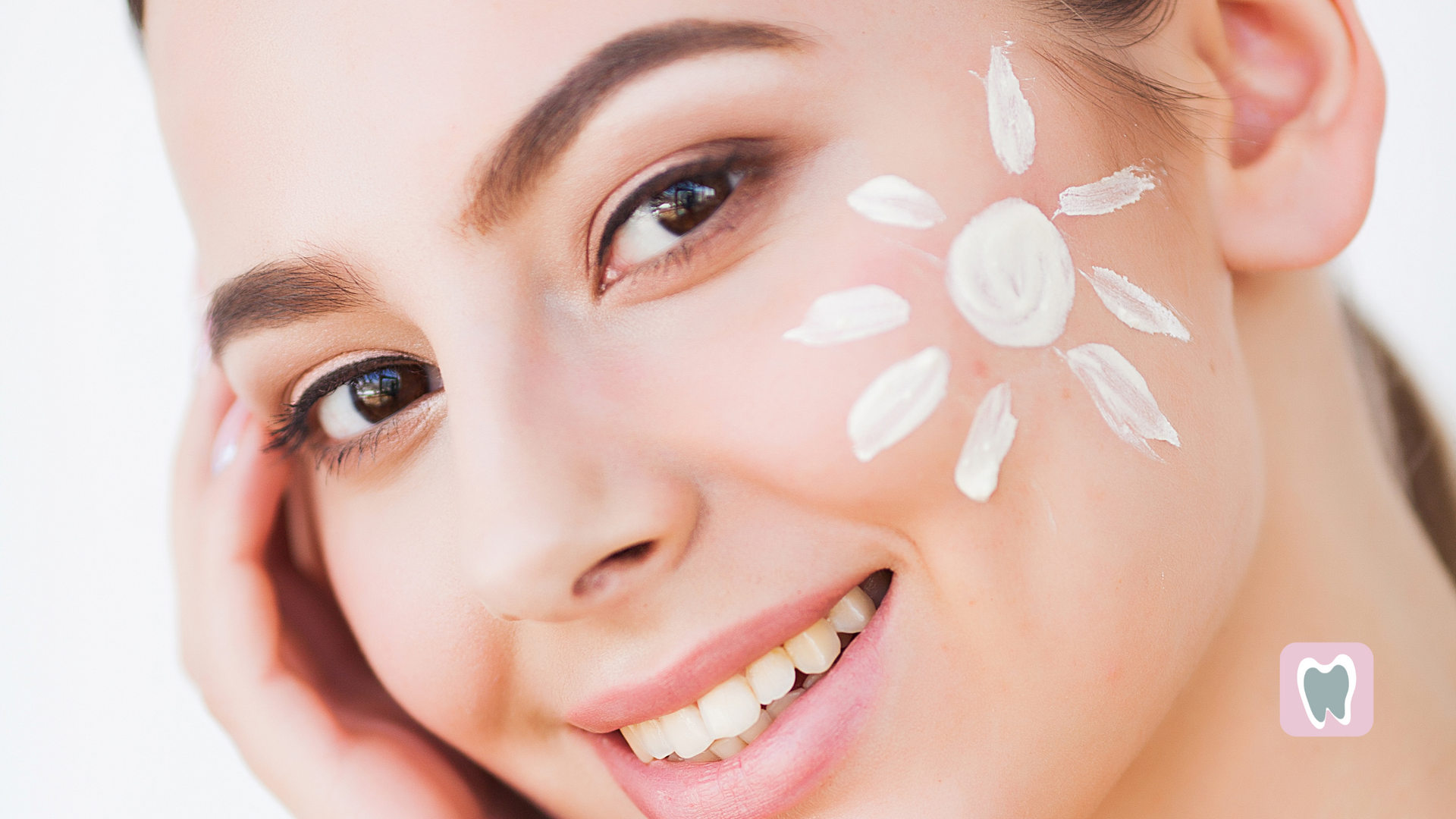 A woman is smiling with sunscreen on her face.