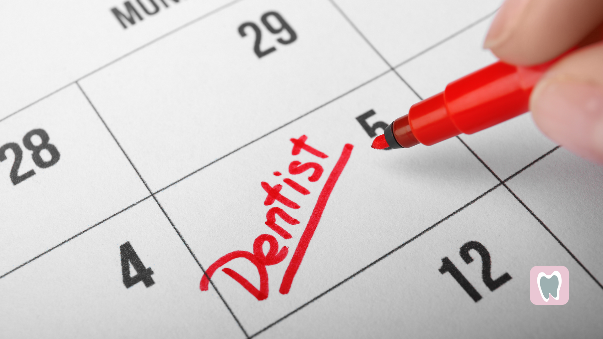 A person is writing the word dentist on a calendar