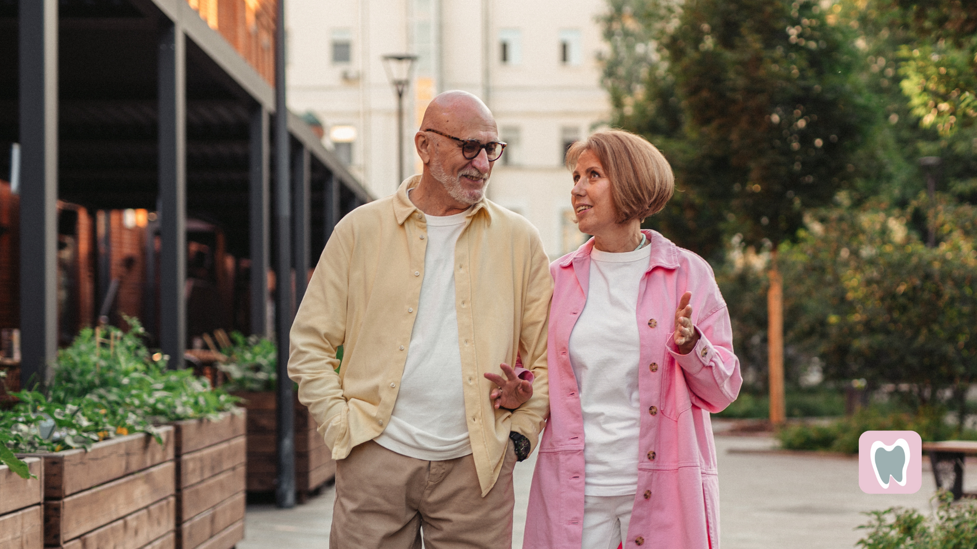 An elderly couple is walking down the street and talking to each other.