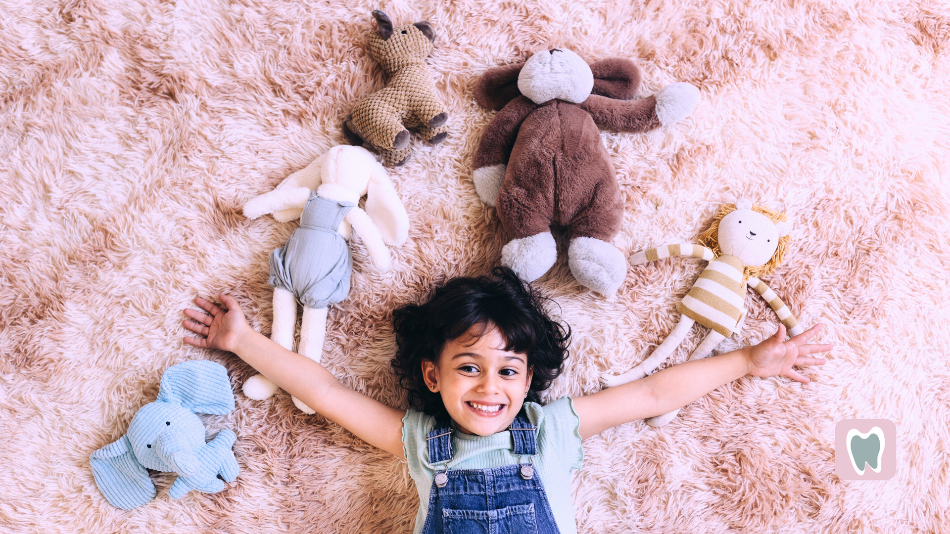 A little girl is laying on the floor surrounded by stuffed animals.