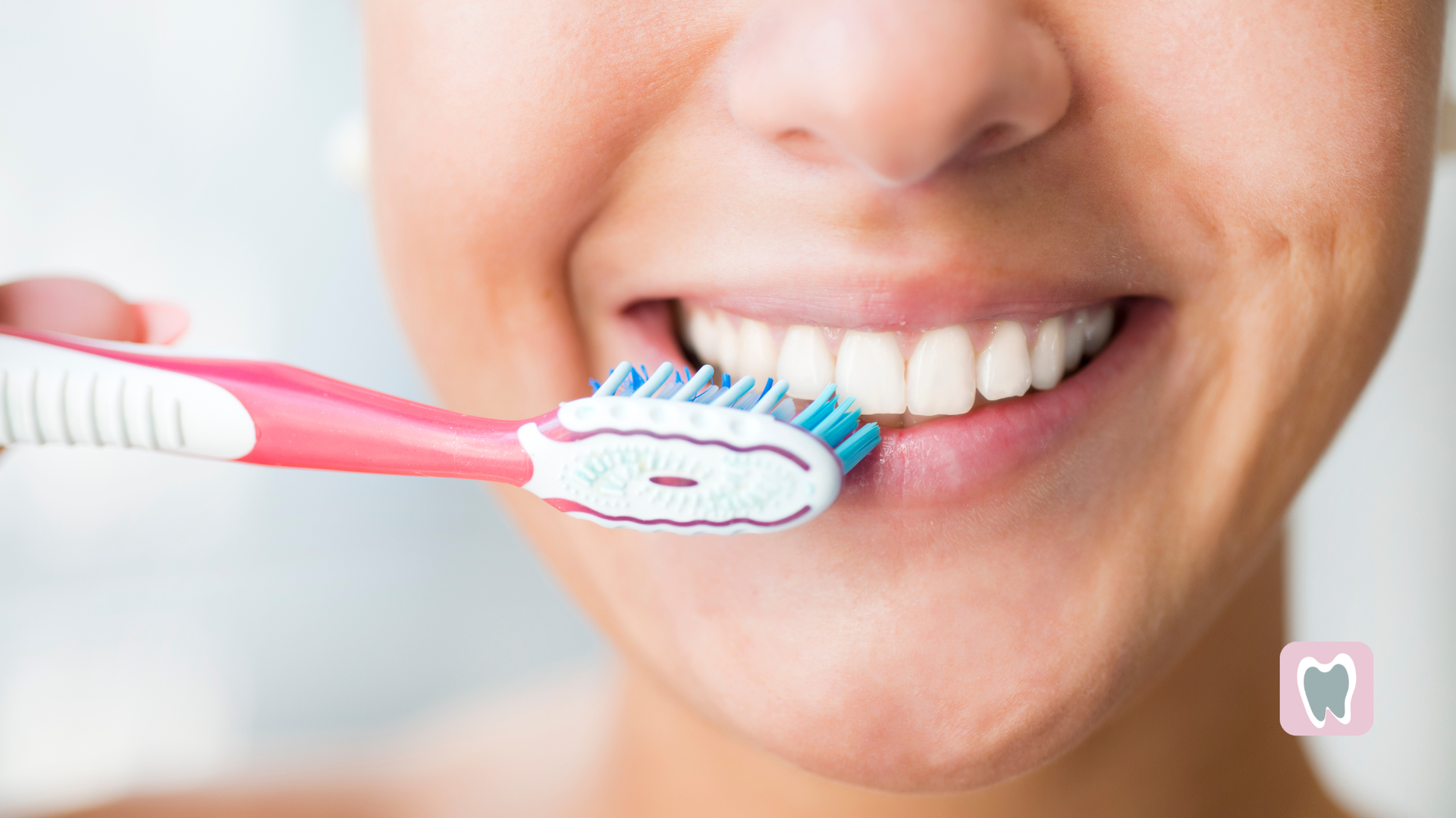 Person brushing teeth with pink toothbrush, smiling, close-up shot.