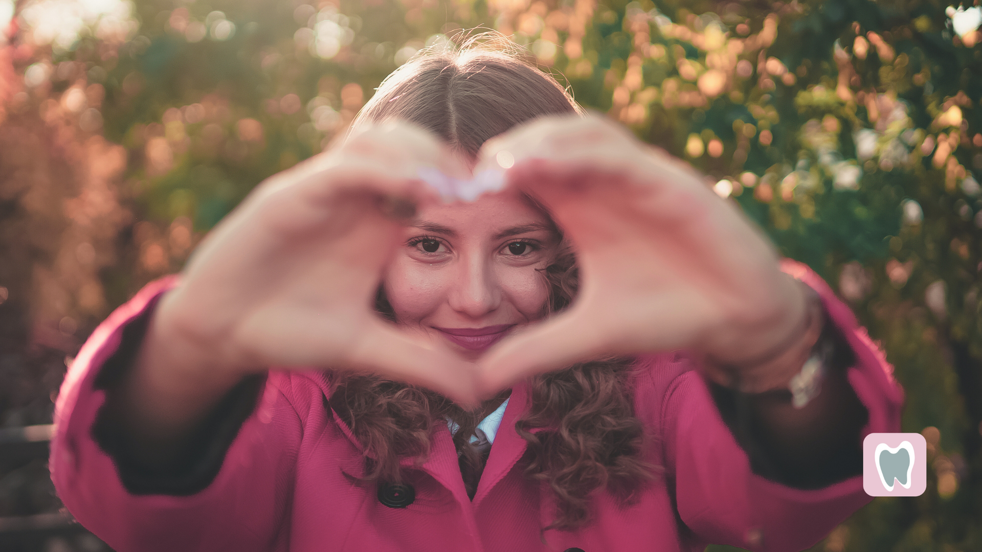 A woman in a pink coat is making a heart shape with her hands.