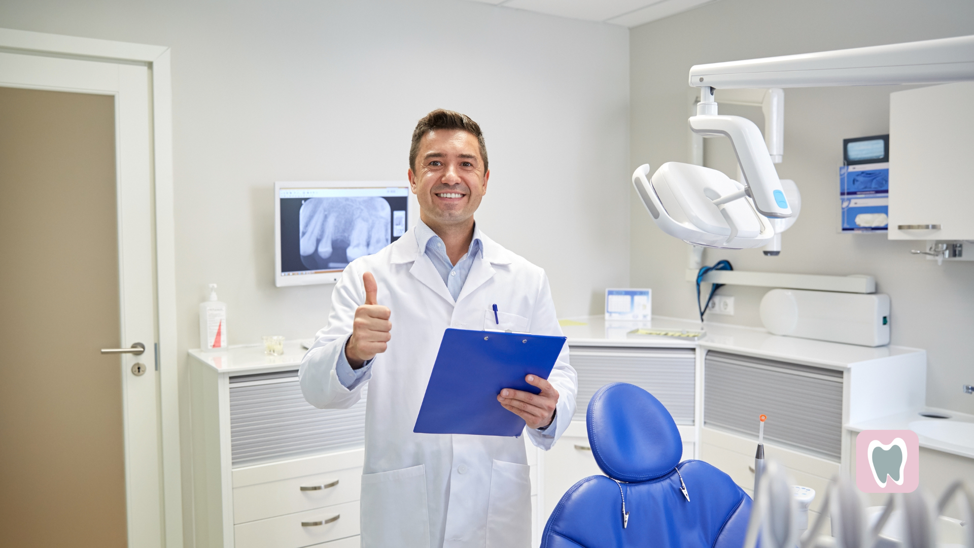 Dentist in white coat gives thumbs up, holding clipboard, in dental office with equipment.