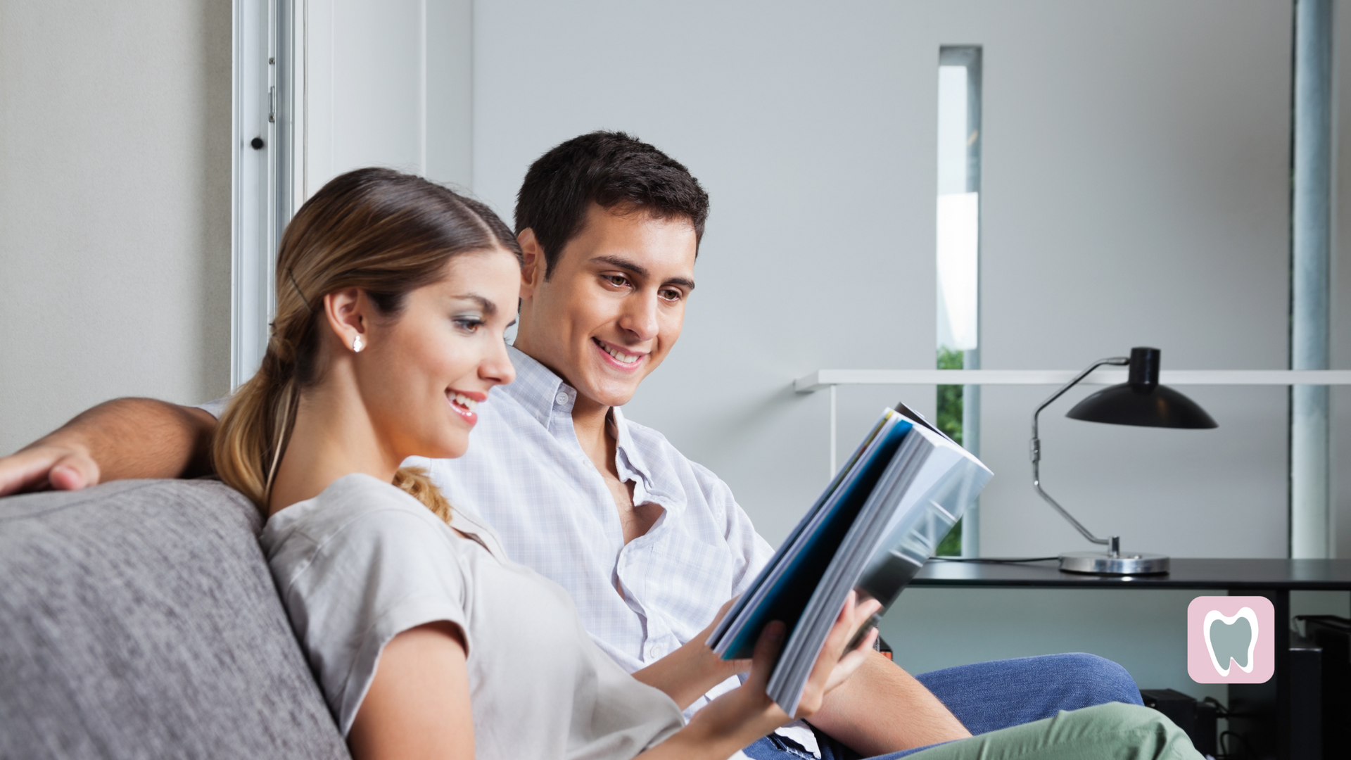 A man and a woman are sitting on a couch reading a book.