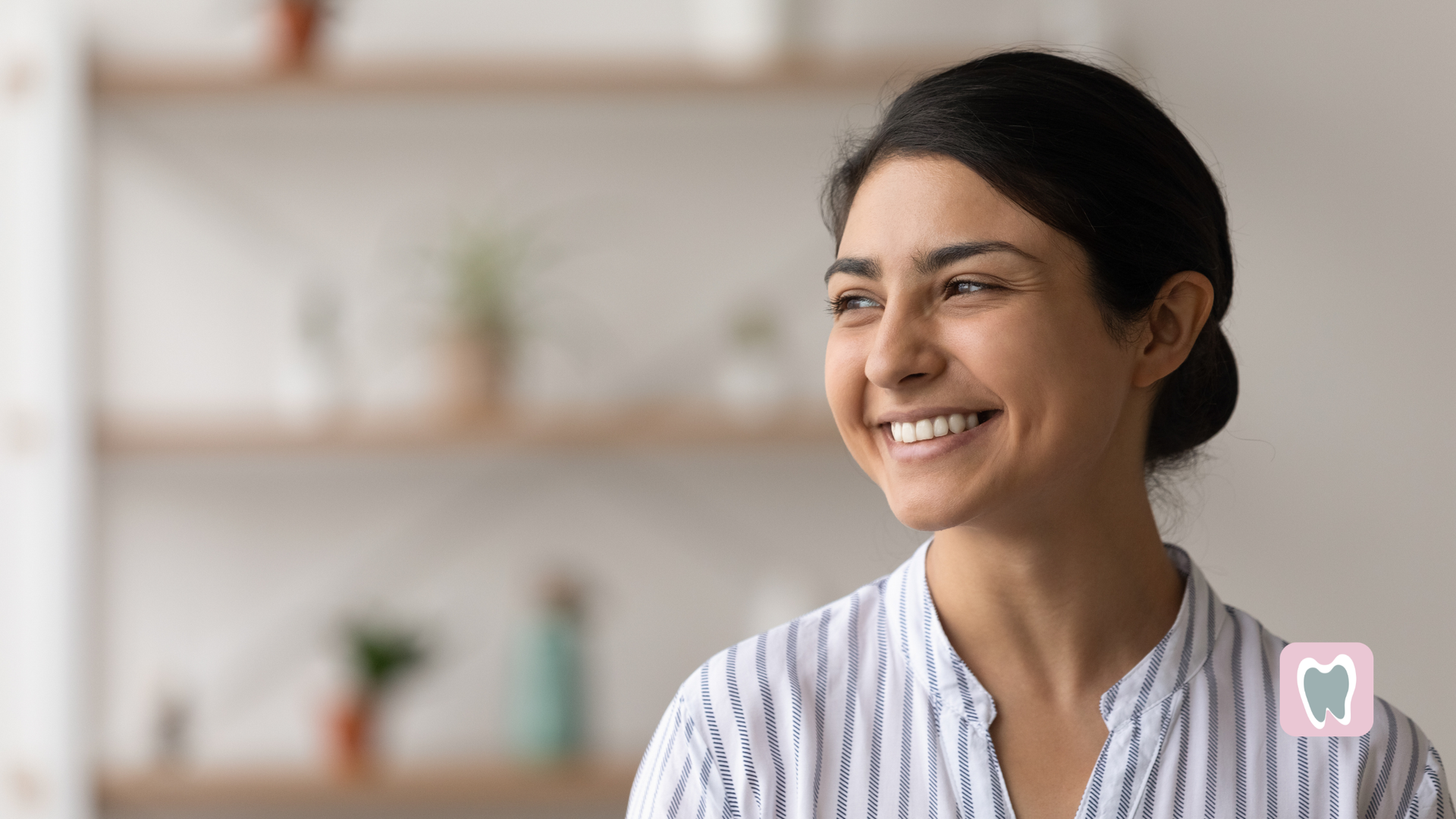 Woman smiling, looking to the side, wearing a striped shirt. Blurred background with shelves.