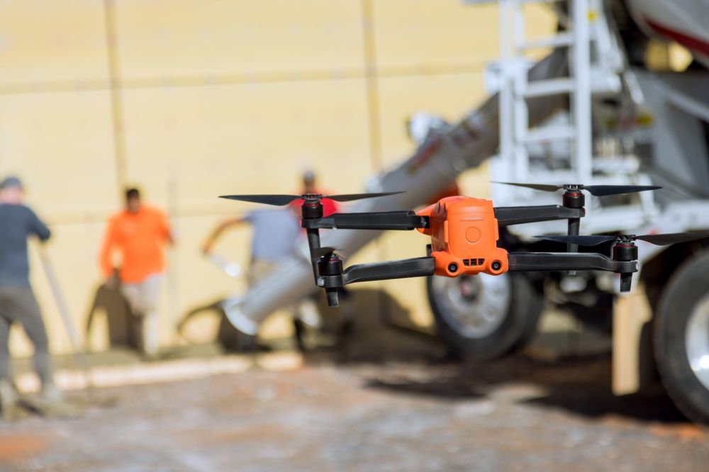 A drone is flying over a construction site in front of a cement truck.