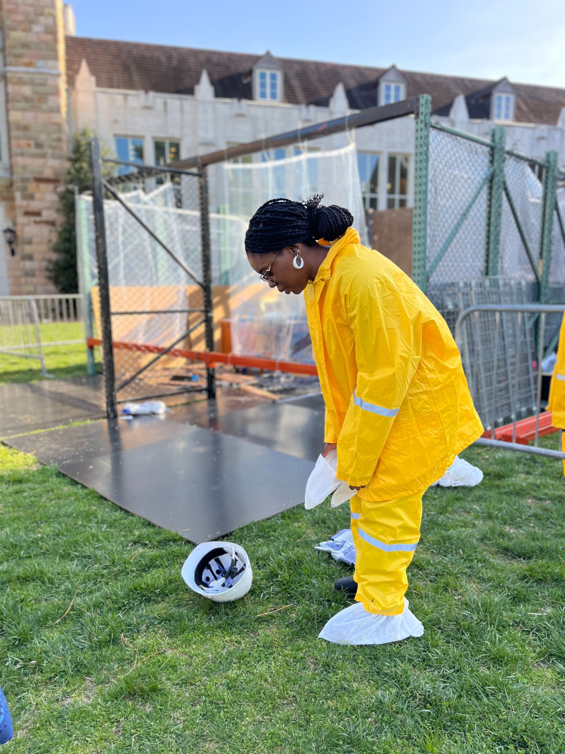 A woman in a yellow raincoat is kneeling on the grass.
