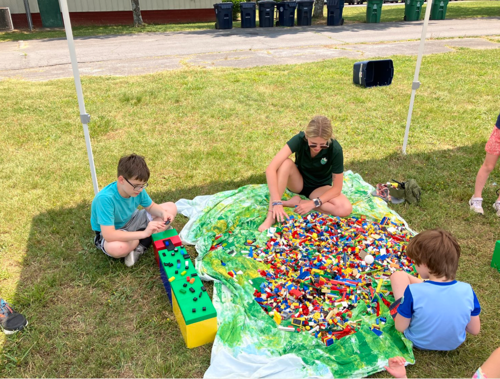 A group of children are sitting on the grass playing with lego blocks.