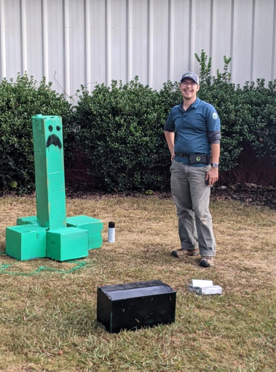 A man is standing next to a giant green creeper in the grass.