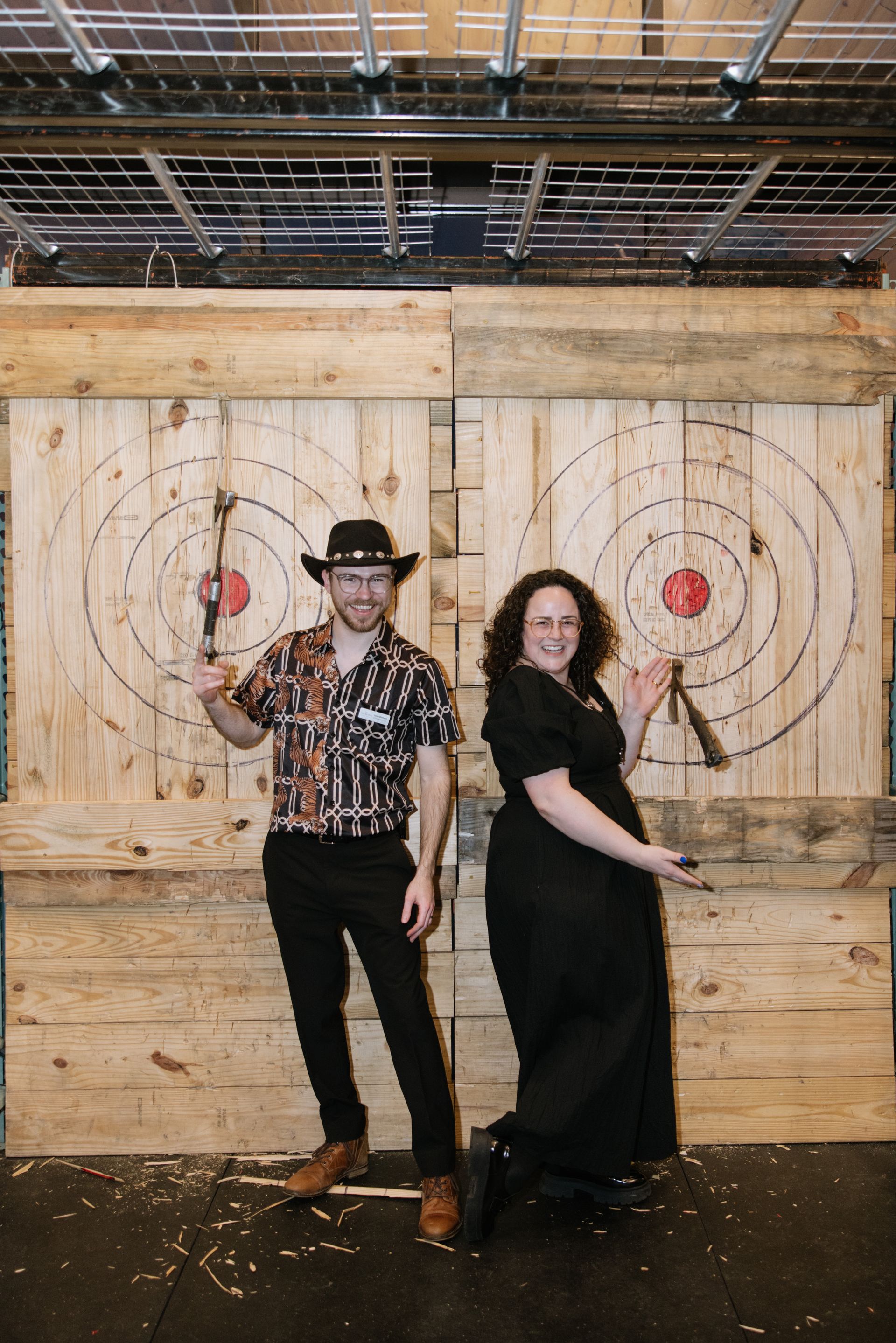 A man and a woman are standing next to each other holding axes in front of a wooden target.