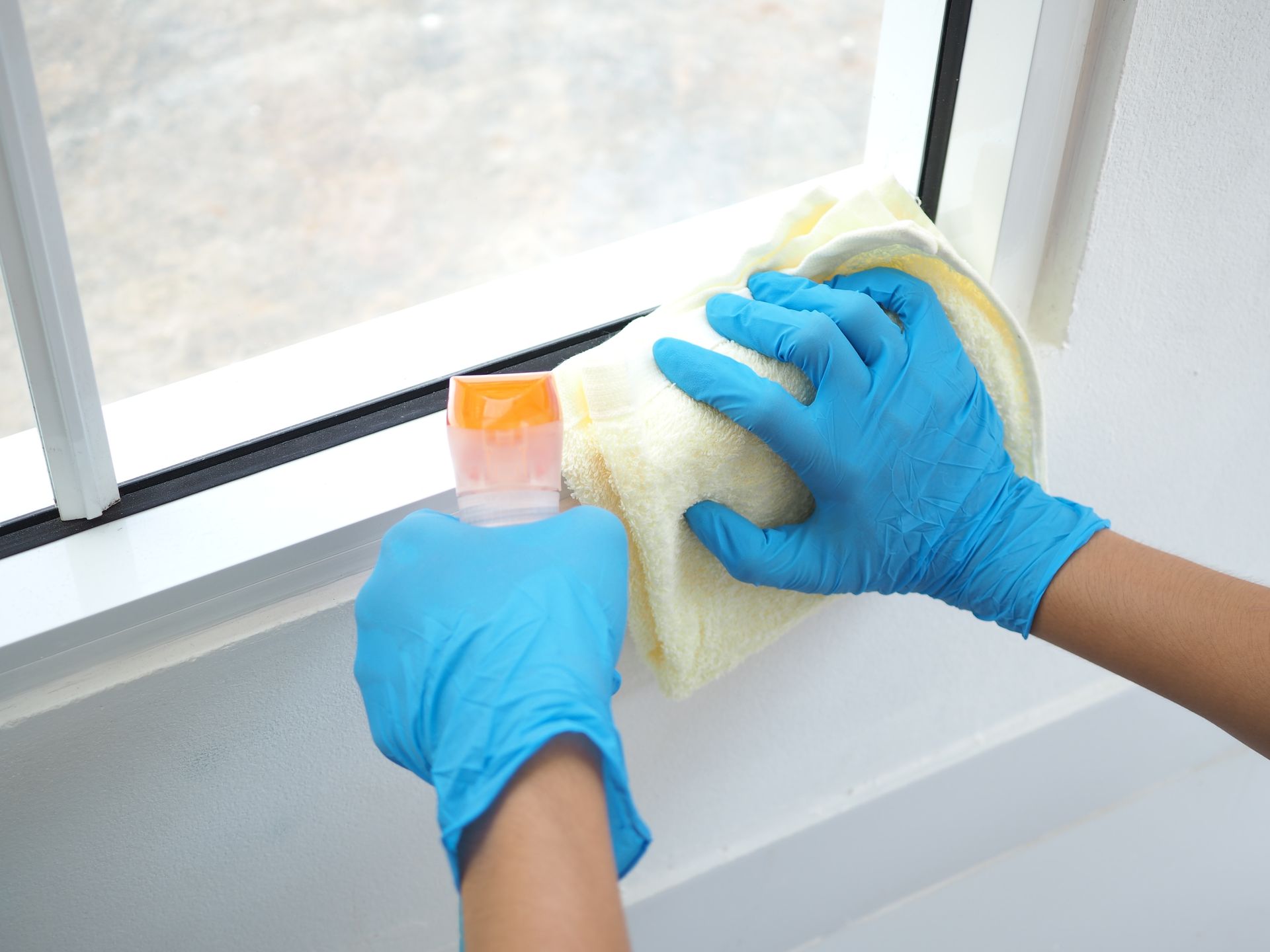 A person wearing blue gloves is cleaning a window with a cloth.