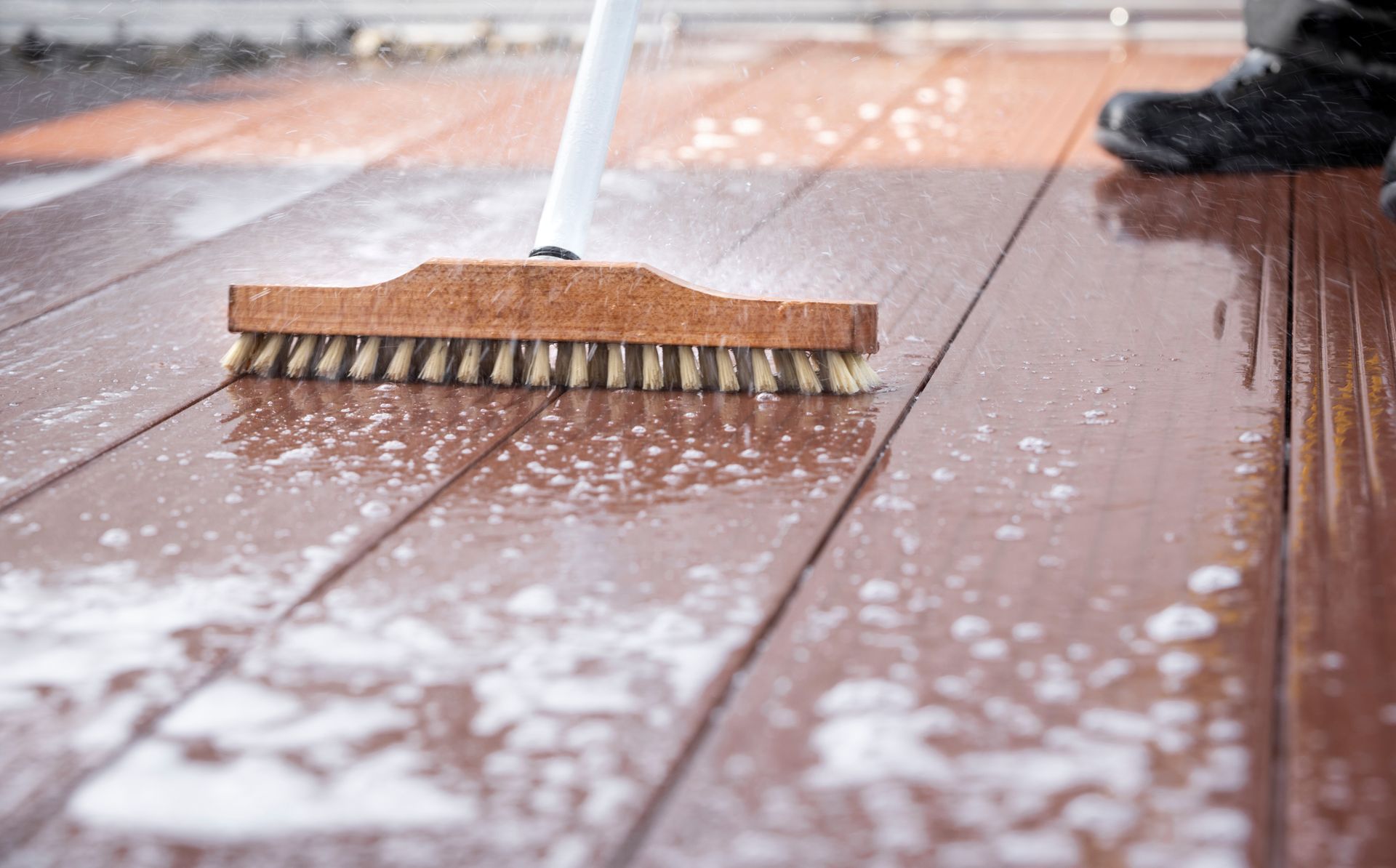 A person is cleaning a wooden deck with a broom.