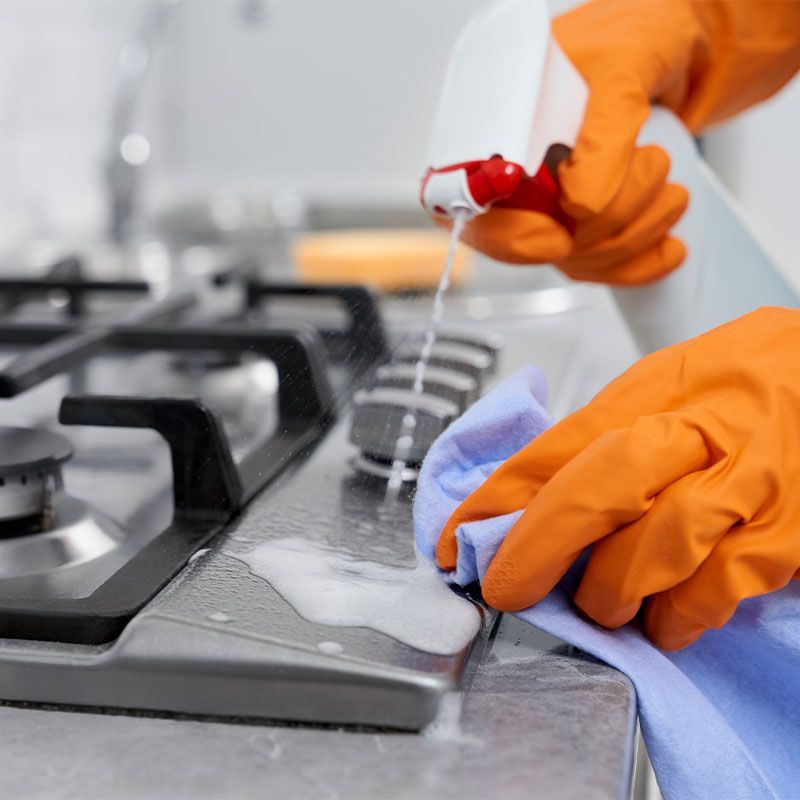 A person is cleaning a gas stove with a spray bottle and a cloth.