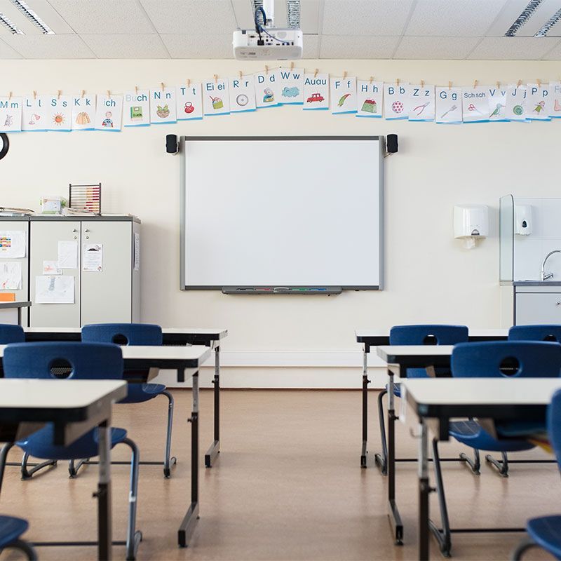 An empty classroom with tables and chairs and a whiteboard.