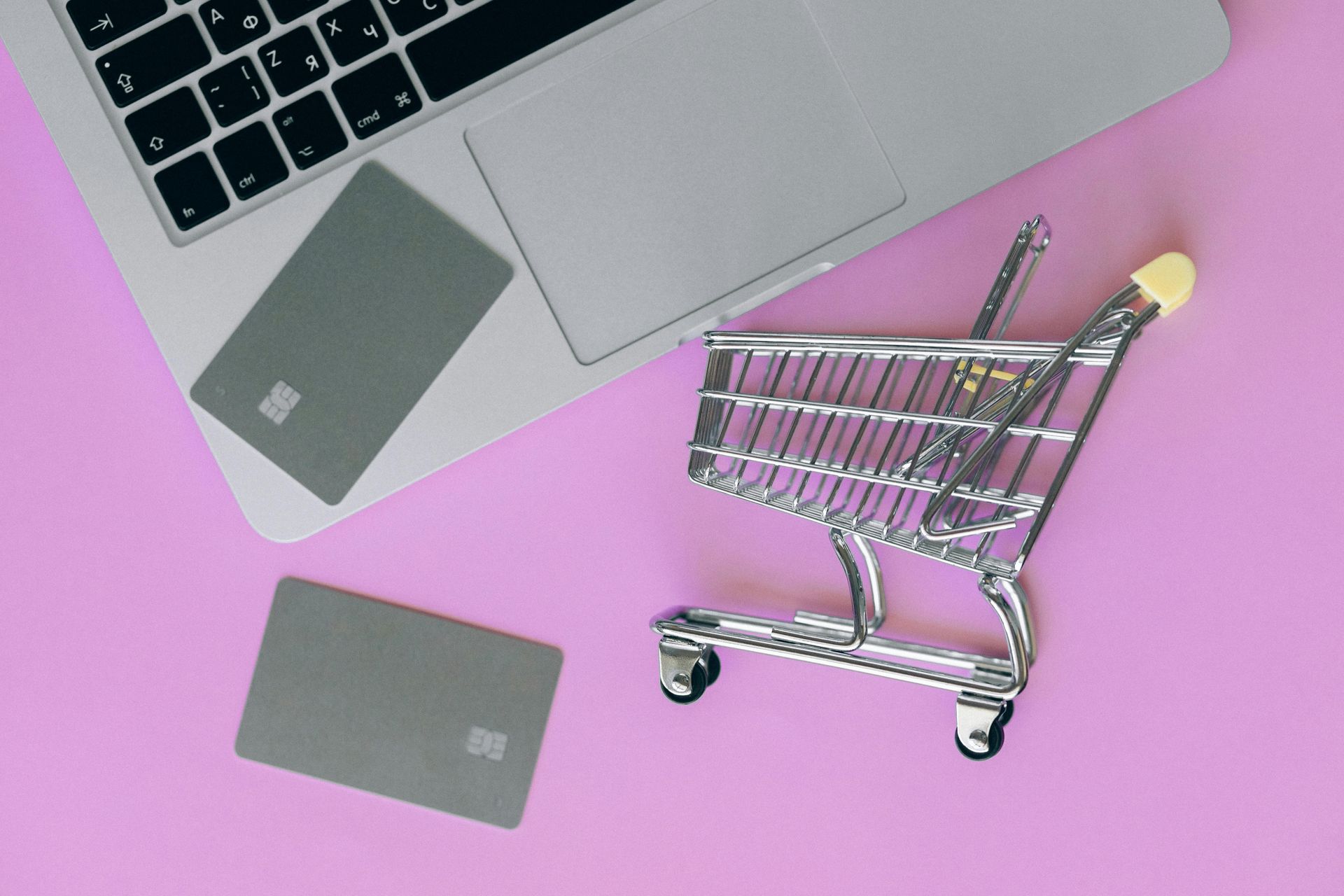 Laptop, shopping cart, and two gray cards on a pink background