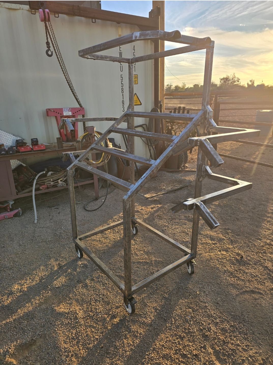 Metal frame structure outdoors on gravel beside a building at sunset