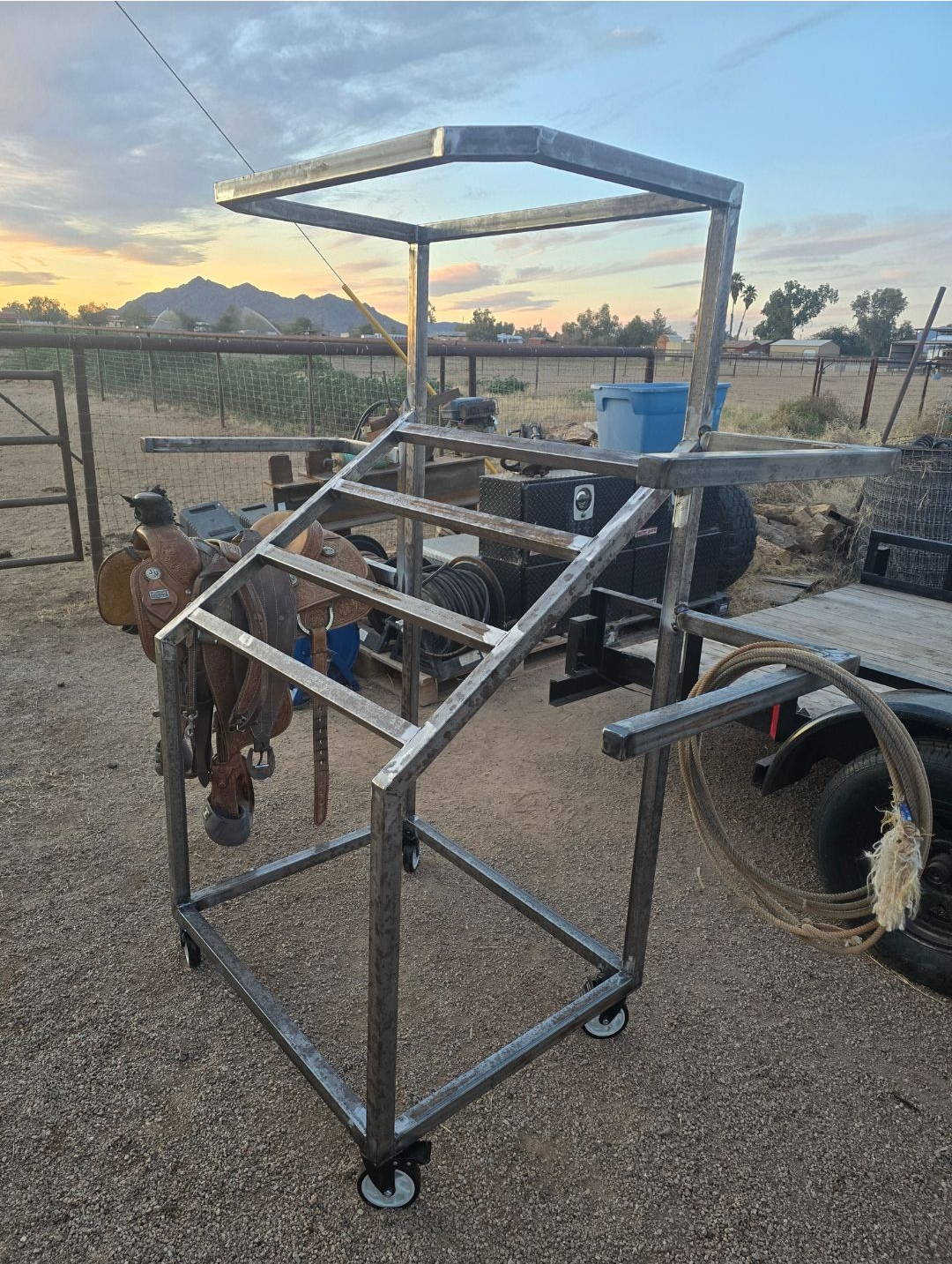 Metal cart frame on wheels in a yard at sunset, with tires and tools in the background.