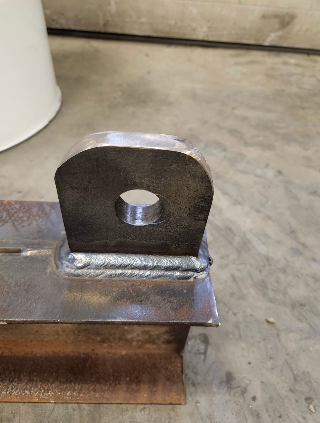 Welded steel bracket with a hole, mounted on a metal plate in a workshop setting
