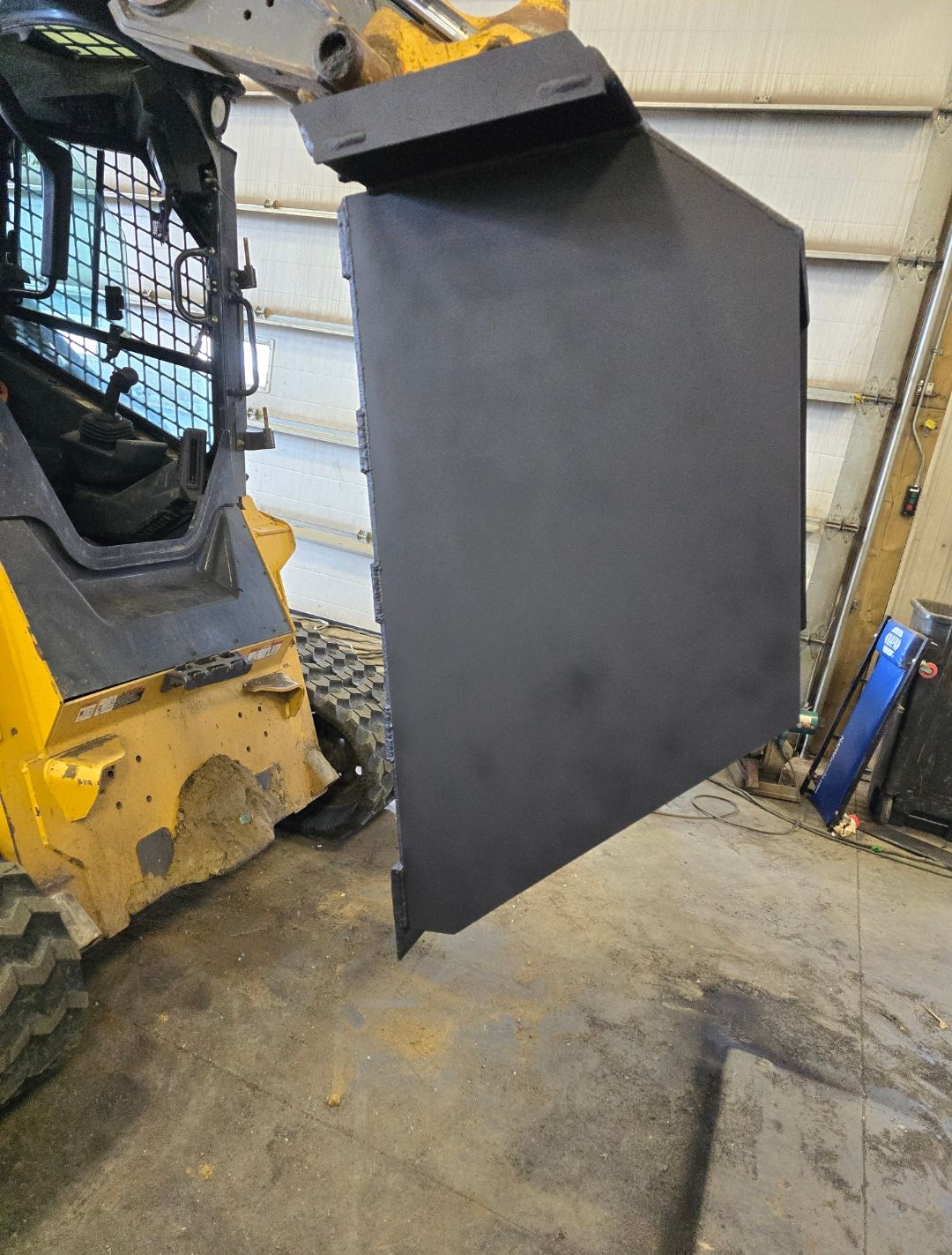 Gray metal panel hanging beside a yellow construction machine inside a workshop