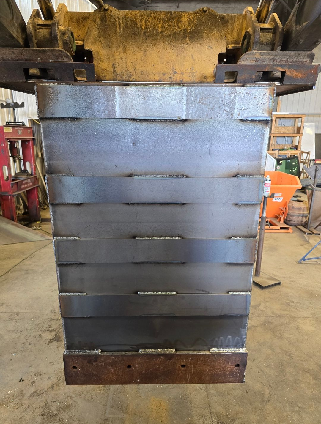 Gray industrial metal hopper or bin with horizontal slats in a workshop setting