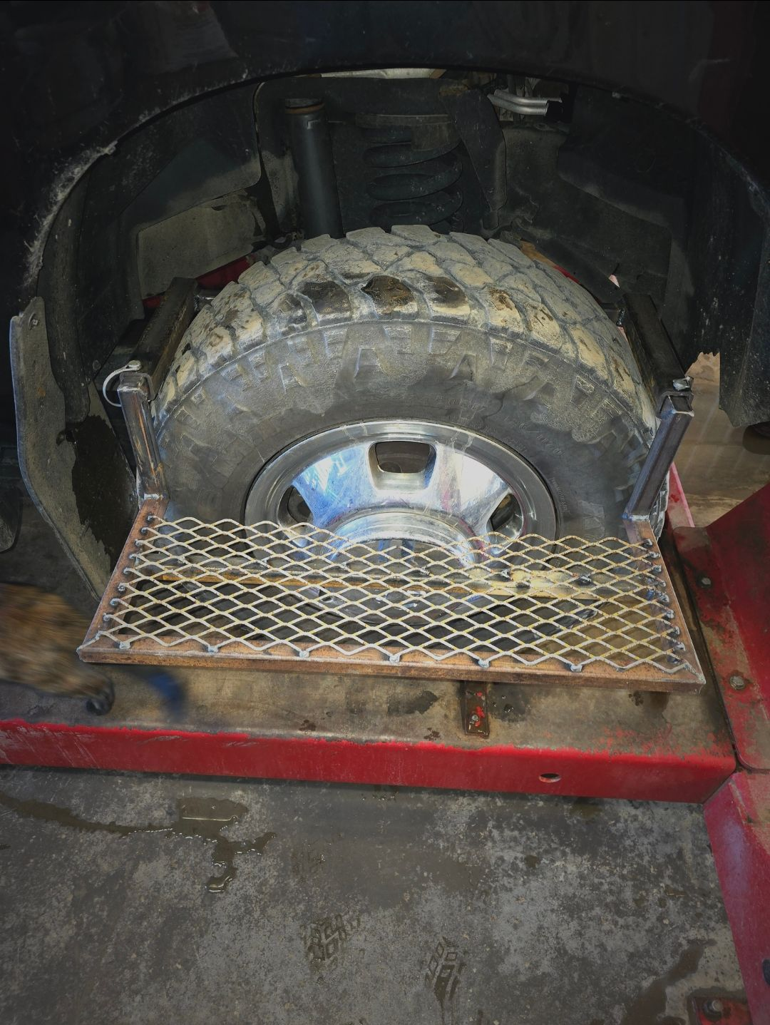 Large off-road tire mounted on a red vehicle inside a dark garage, beside a metal platform.