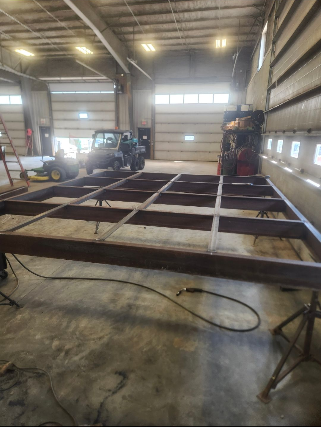 Large steel frame on a warehouse floor with a forklift in the background and a hose in the foreground.