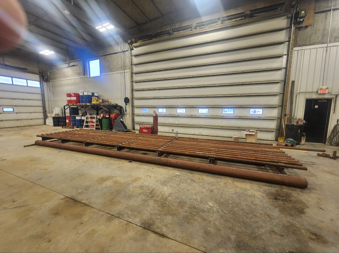Industrial workshop with a large metal truss on the floor beside a garage door and equipment