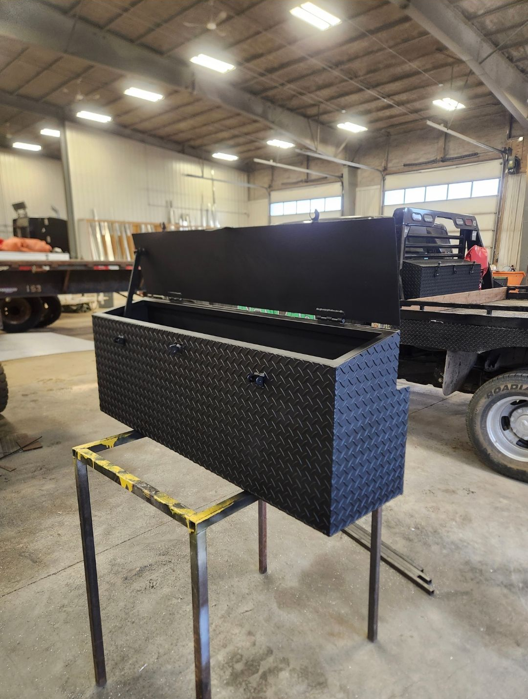 Black metal storage chest with open lid on a stand inside a warehouse garage.