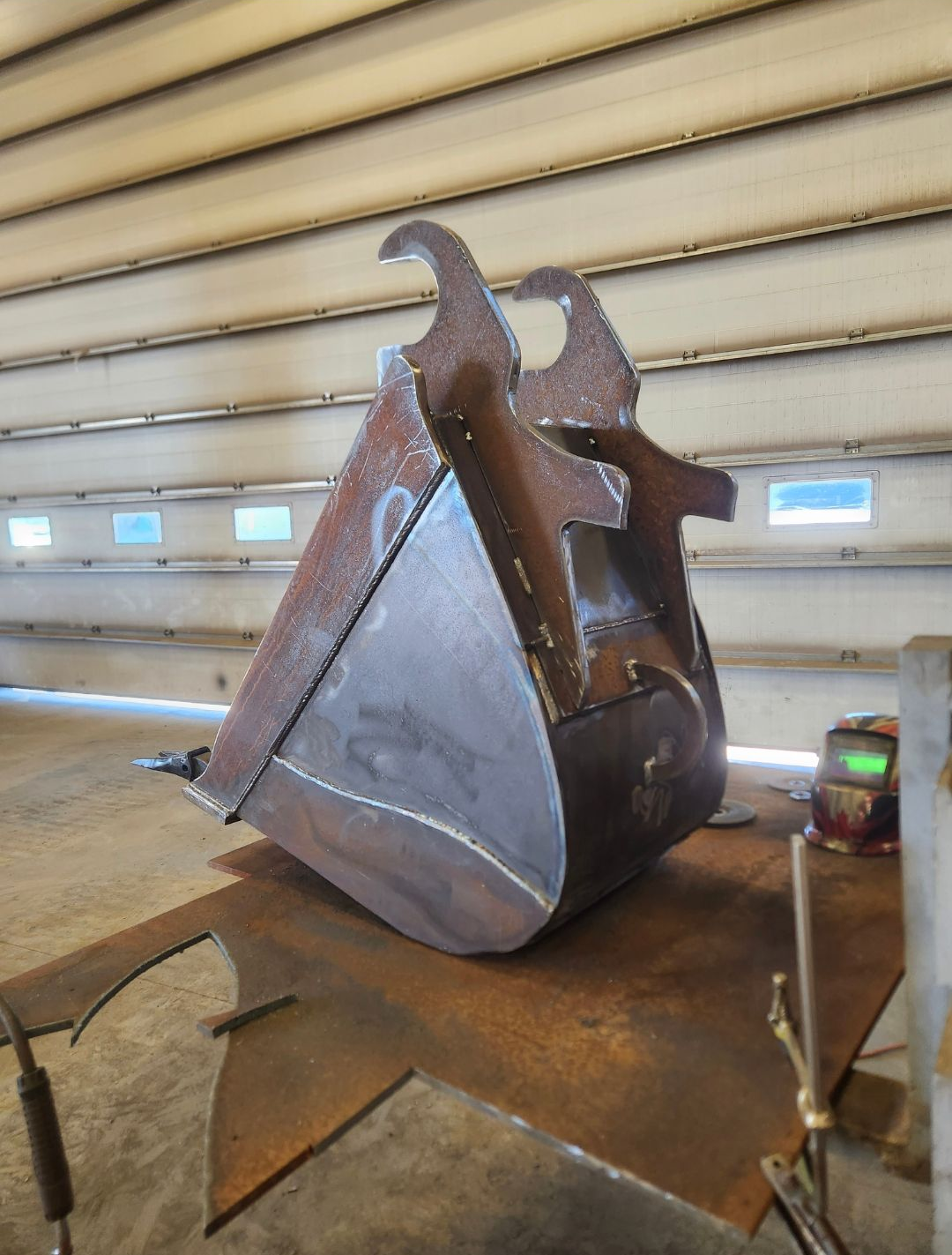 Rusty metal sculpture with a triangular silver panel in a workshop setting